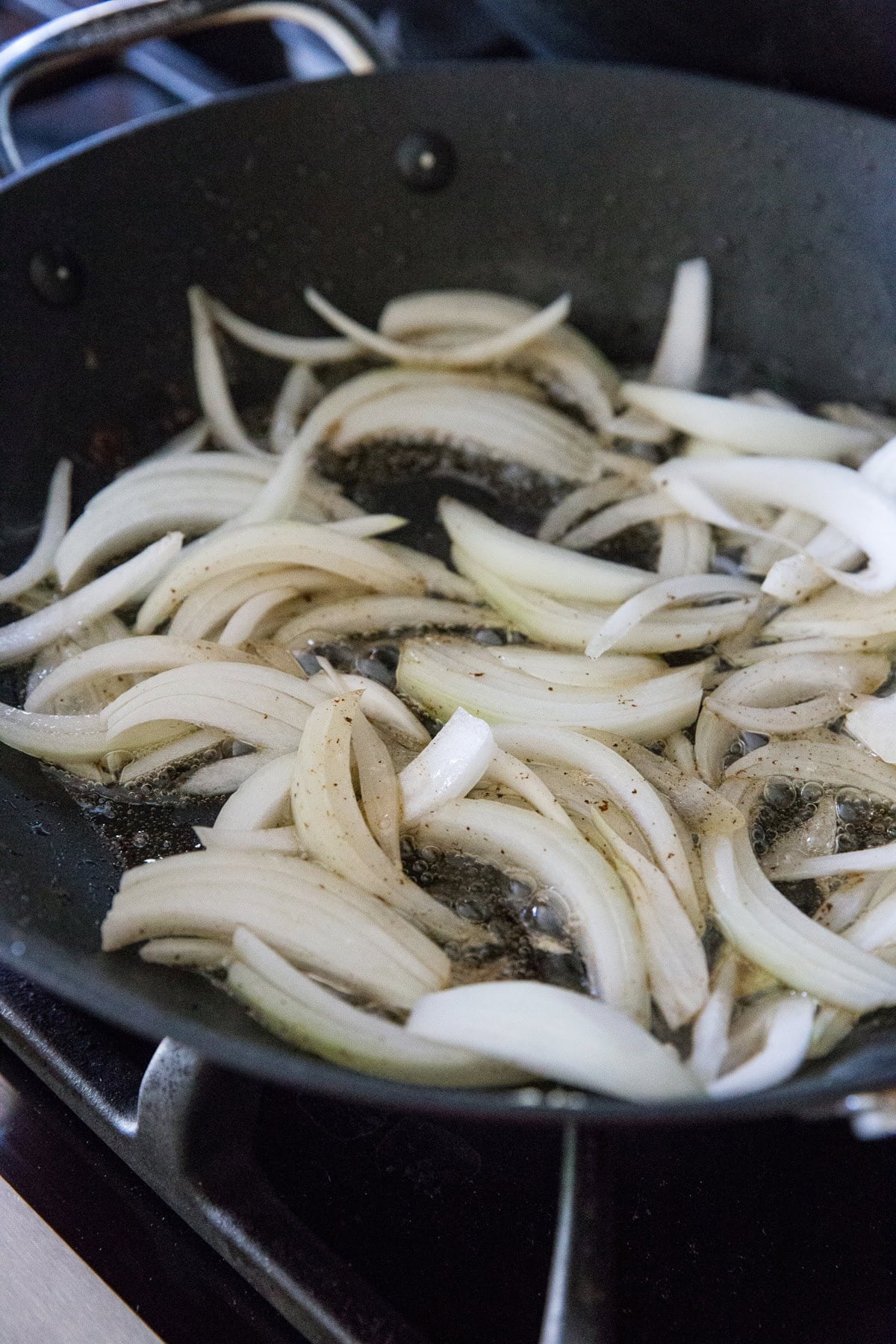 Skillet on a stove top sautéing slices of onion in bacon fat.