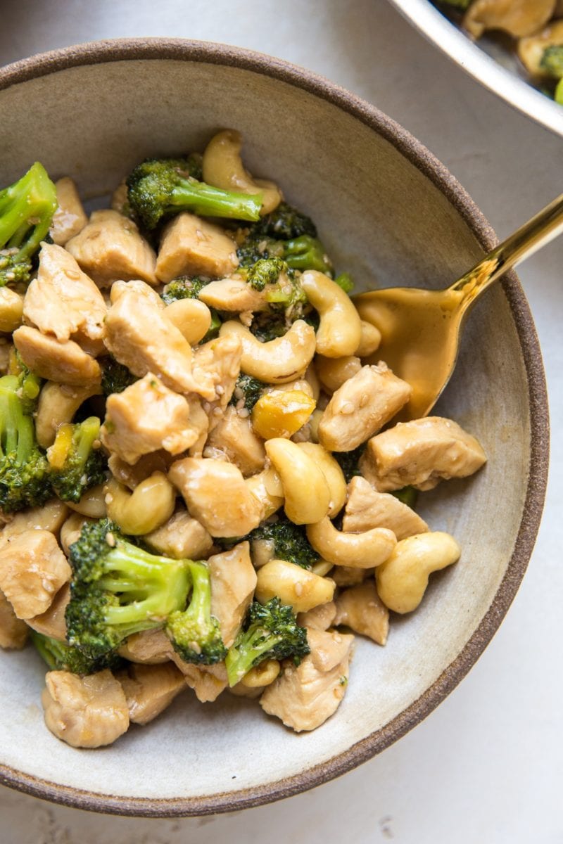 Big bowl of cashew chicken with broccoli, with a golden spoon. Ready to eat.