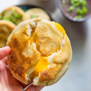A blue plate with four golden, pan-fried cheese pupusas garnished with chopped green onions and cilantro. Salsa and refried beans are in bowls nearby, along with scattered herbs on a white surface—a tempting cheese pupusa recipe.