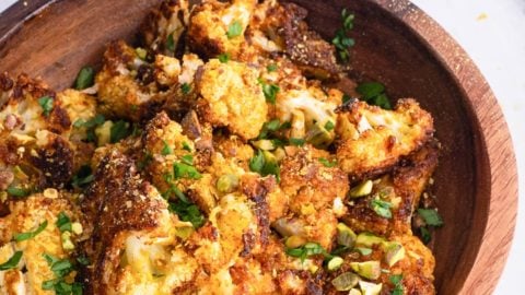 Wooden bowl full of cheesy vegan roasted cauliflower sprinkled with pistachios and ready to serve.