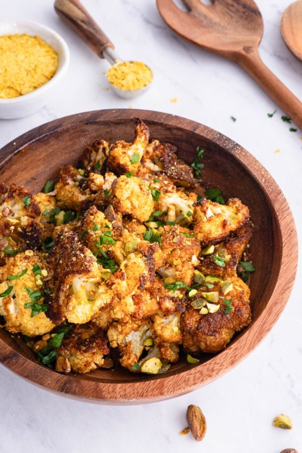 Wooden bowl full of cheesy vegan roasted cauliflower sprinkled with pistachios and ready to serve.