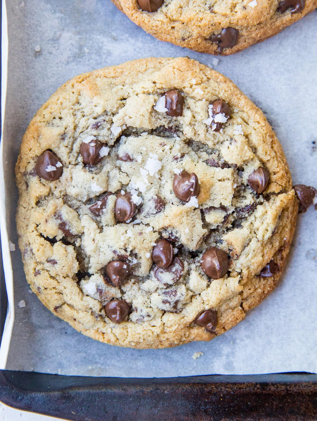 One huge chocolate chip cookie on a baking sheet lined with parchment paper, fresh out of the oven.