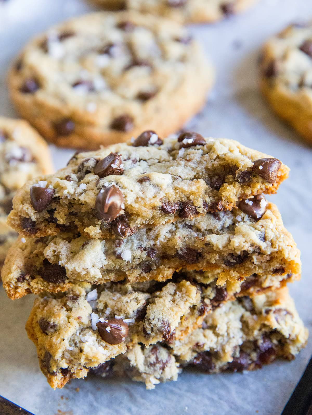 Stack of chewy keto chocolate chip cookies broken in half on a cookie sheet so you can see the gooey center and the golden brown edge.