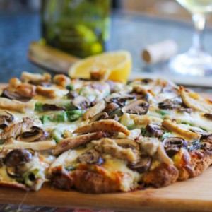 Pesto chicken pizza cut into slices on a cutting board.