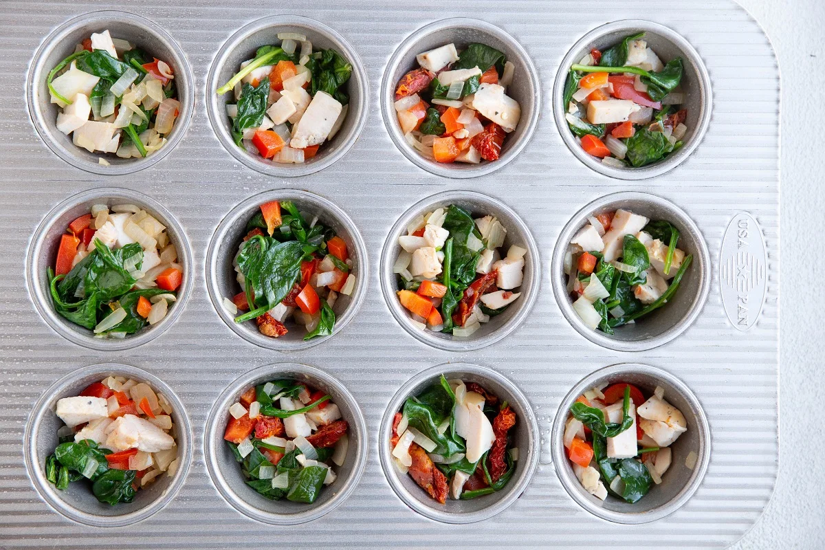 Chicken and vegetables inside muffin holes of a muffin tray for egg cups.