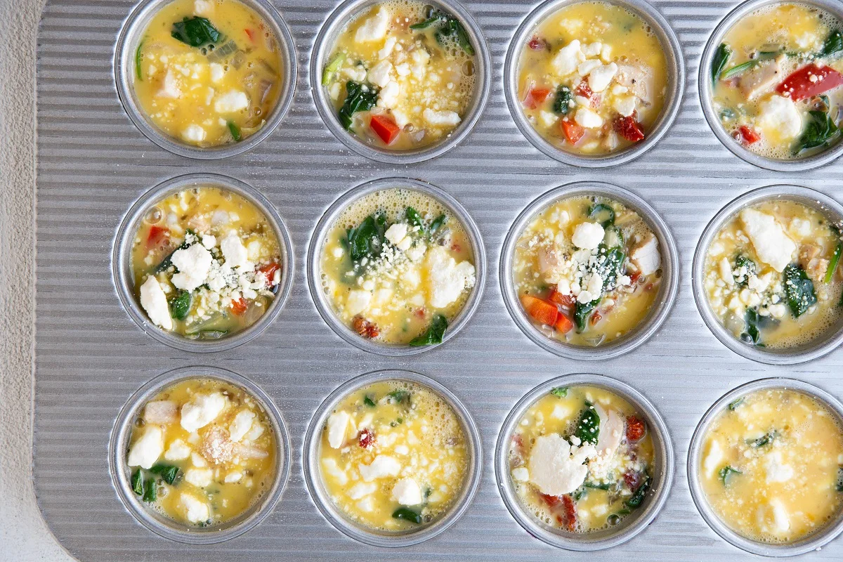 Egg cups ready to go into the oven with raw eggs and feta cheese on top.