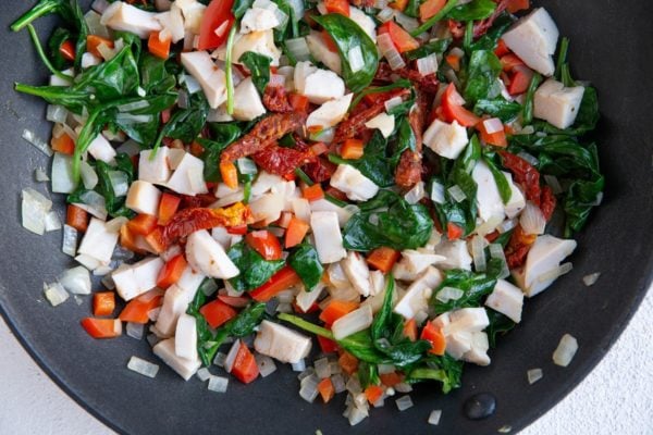 Skillet with onion, bell pepper, chicken, sun-dried tomatoes and spinach in it.