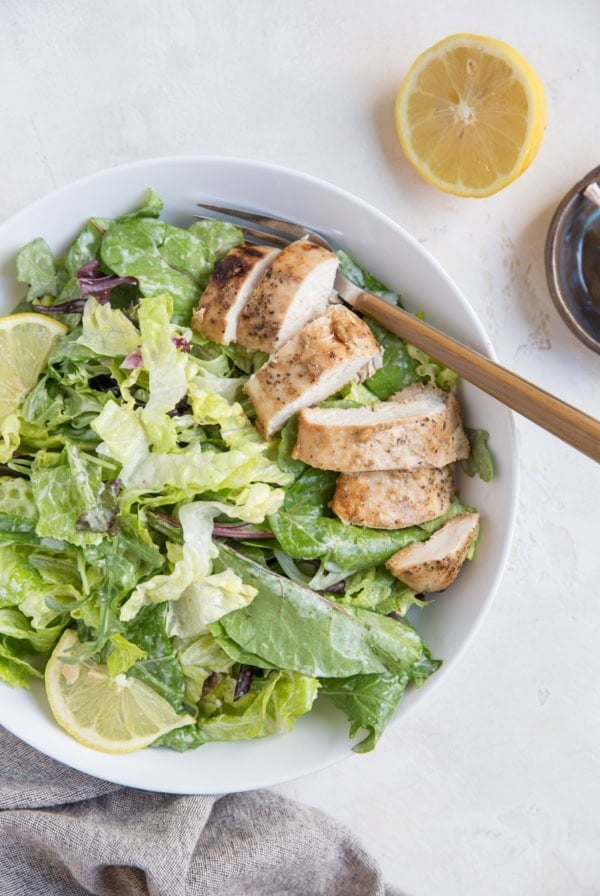 Balsamic Baked Chicken Caesar Salad in a bowl with a napkin and half a lemon