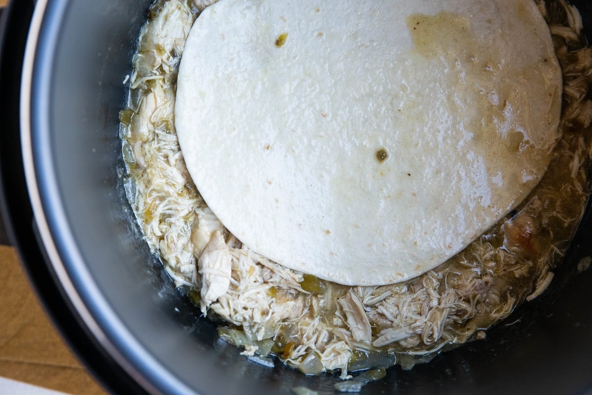 Tortilla being dipped into saucy shredded chicken to wet the tortillas