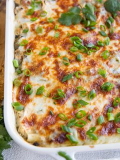 Casserole dish of green chicken enchiladas sprinkled with green onion