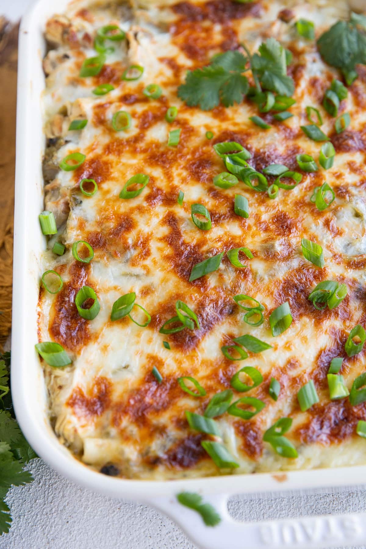 Casserole dish of green chicken enchiladas sprinkled with green onion