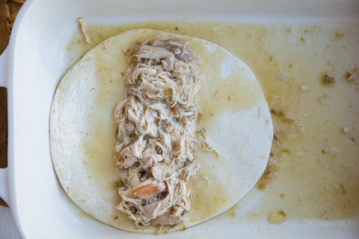 baking dish with one enchilada being made - a tortilla with shredded chicken in the middle