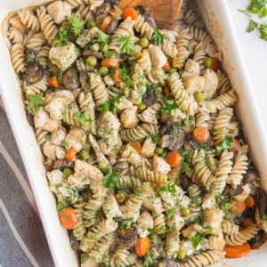 Casserole dish full of chicken noodle casserole with mushrooms, peas, and carrots.