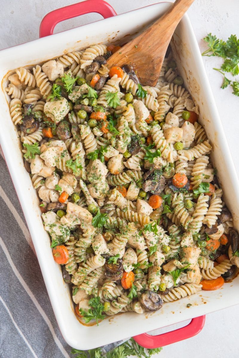 Casserole dish full of chicken noodle casserole with mushrooms, peas, and carrots.