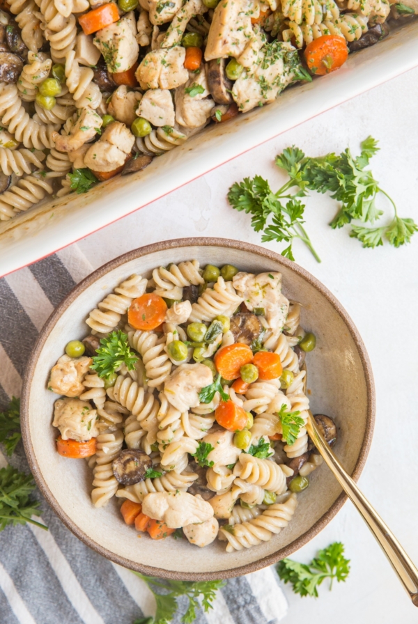 Creamy Chicken Noodle Casserole in a bowl with a golden spoon and a napkin with fresh parsley to the side.