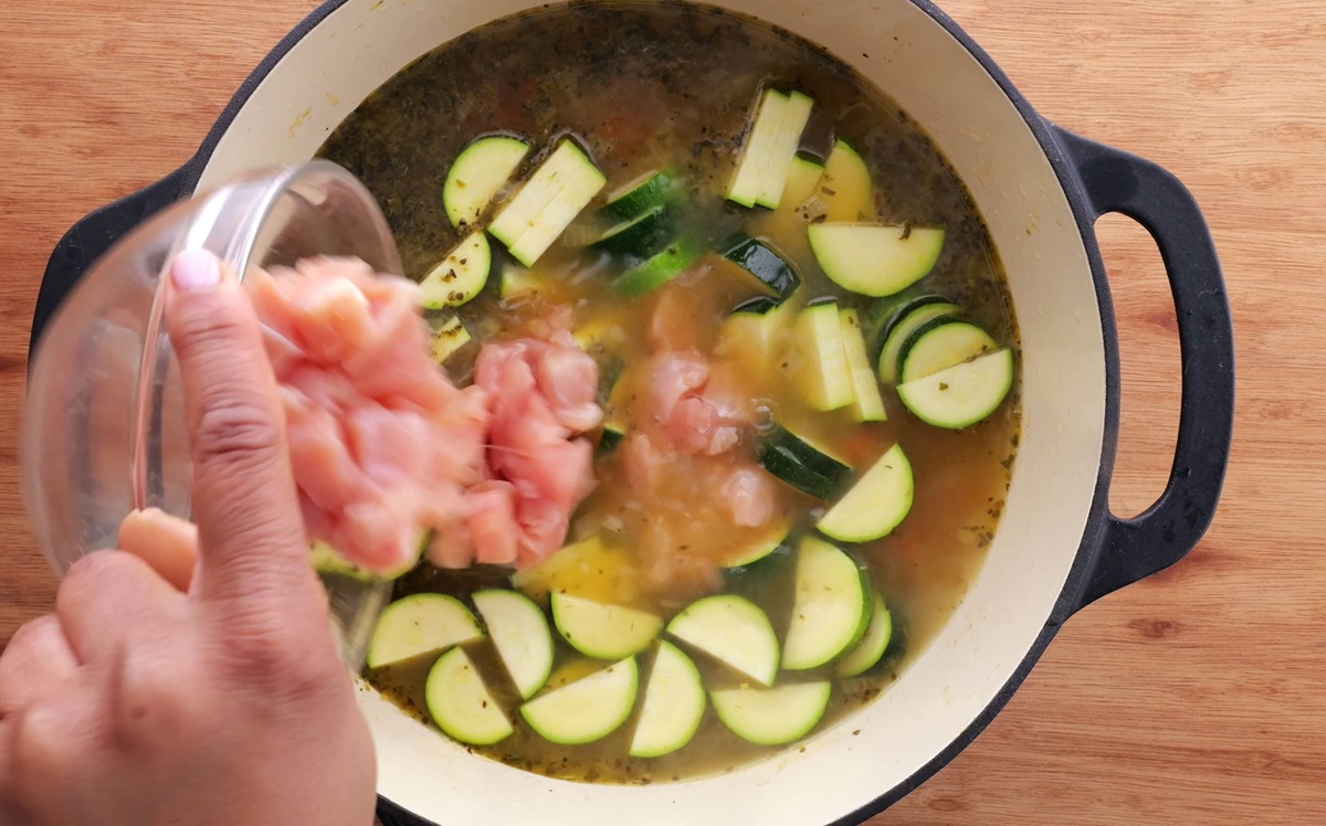 Pouring chopped zucchini and chopped chicken breasts into a large soup pot.