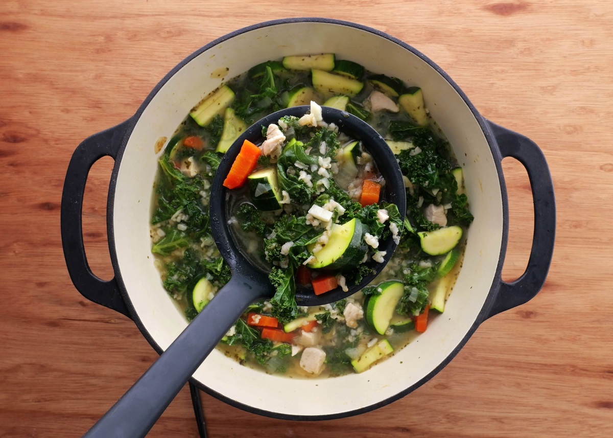Big pot of chicken soup with rice and kale. Freshly made with a ladle taking a scoop out to serve.