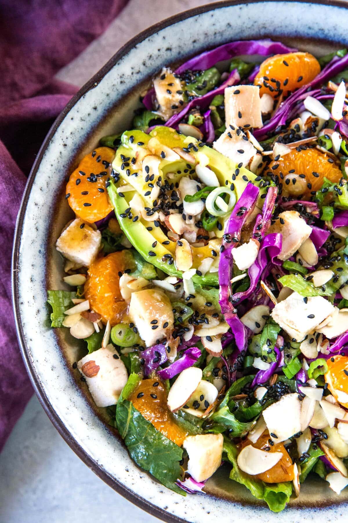 Paleo Chinese Chicken Salad in a huge salad bowl with spinach and soy-free sesame ginger dressing with mandarins, avocado, and sliced almonds.