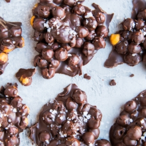 Chocolate Covered Chickpeas formed into lumps on a blue backdrop, sprinkled with sea salt.