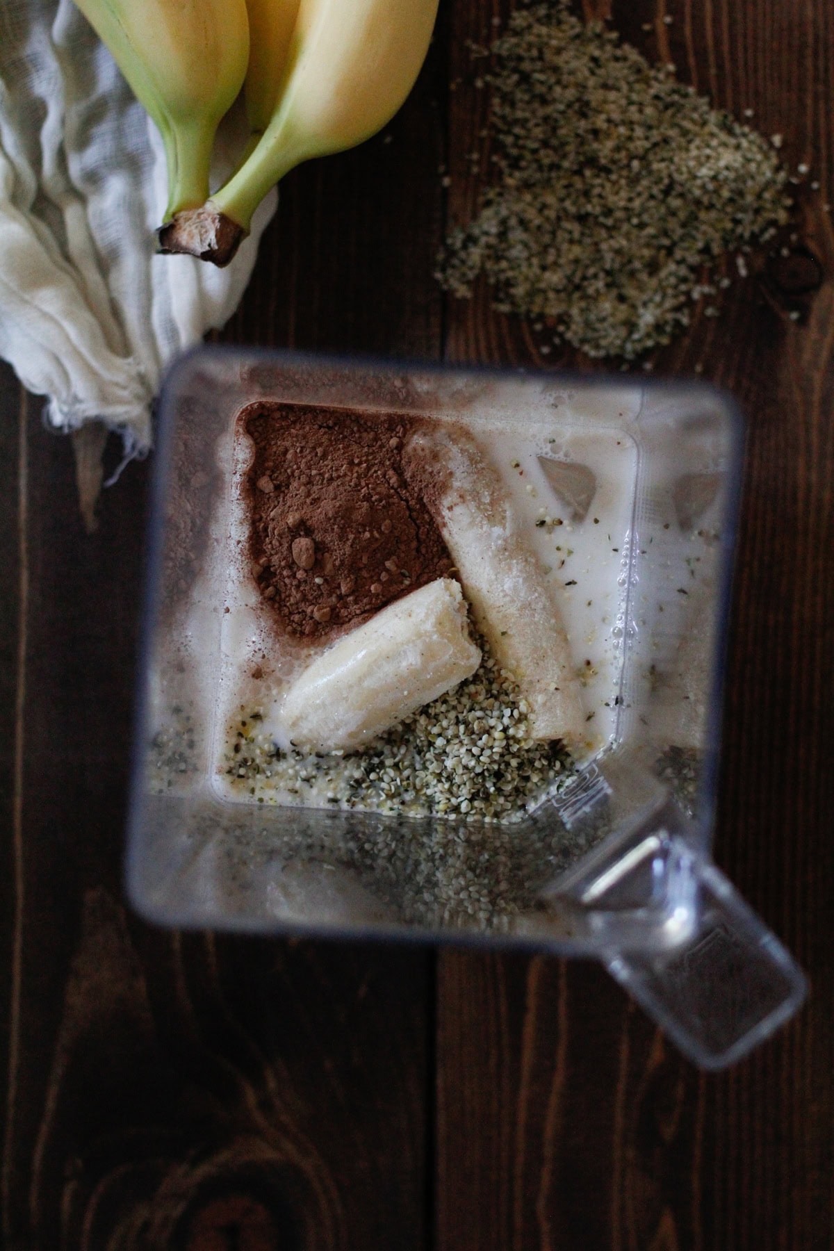 Ingredients for chocolate hemp seed smoothie in a blender with more ingredients around. Ready to blend.