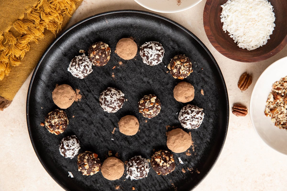 Chocolate truffles on a black plate, rolled in cocoa powder, coconut, and chopped pecans