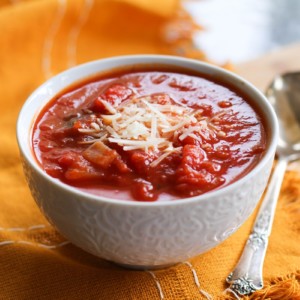 White bowl of tomato soup with a napkin and a spoon, ready to eat.