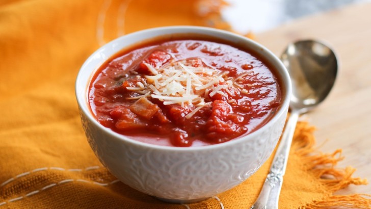 White bowl of tomato soup with a napkin and a spoon, ready to eat.