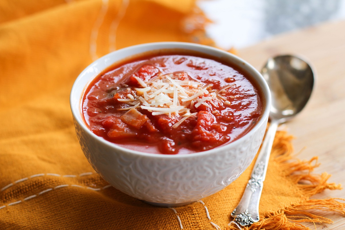 White bowl of tomato soup with a napkin and a spoon, ready to eat.