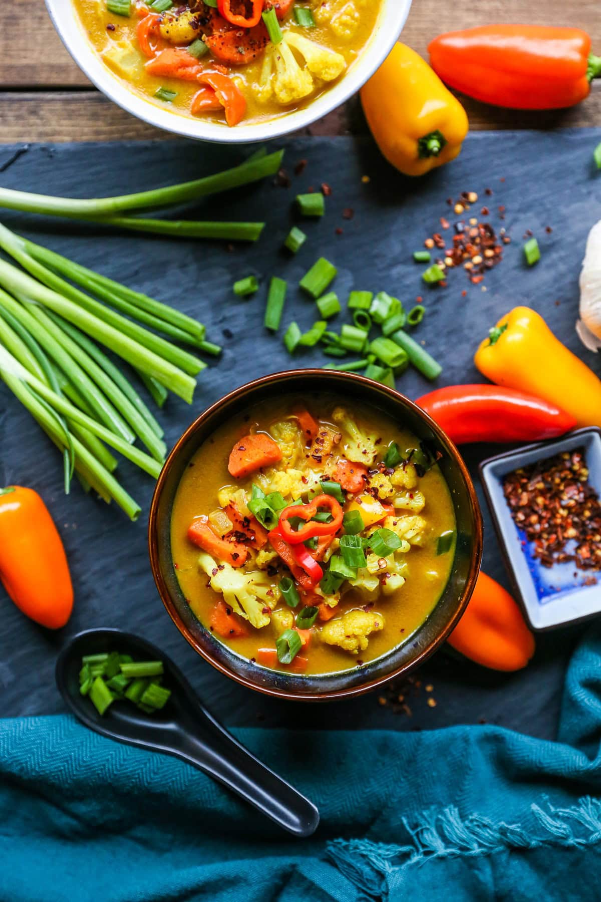 Two bowls of vegetable curry soup with a blue napkin and spoons to the side.