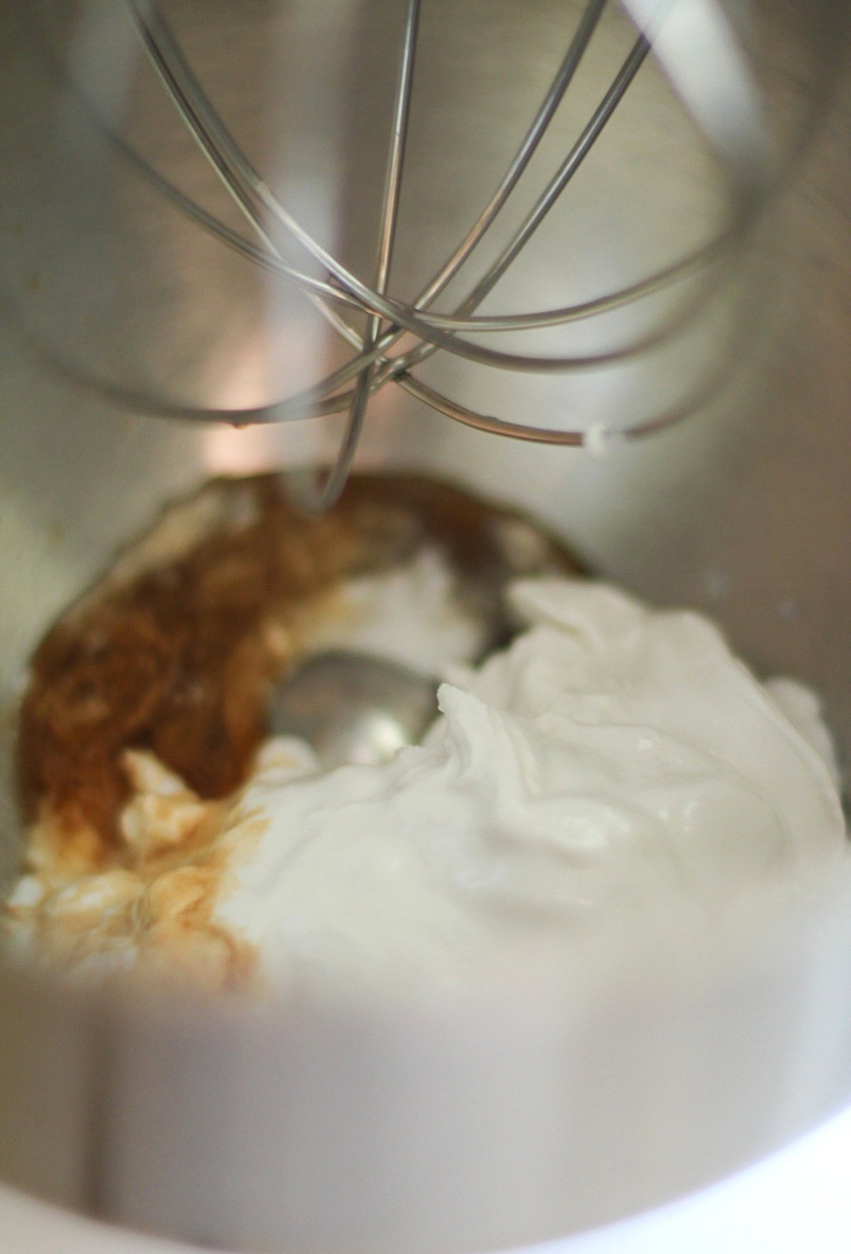 A close-up of a stand mixer bowl containing coconut whipped cream and pure maple syrup, ready to be mixed with a whisk attachment.