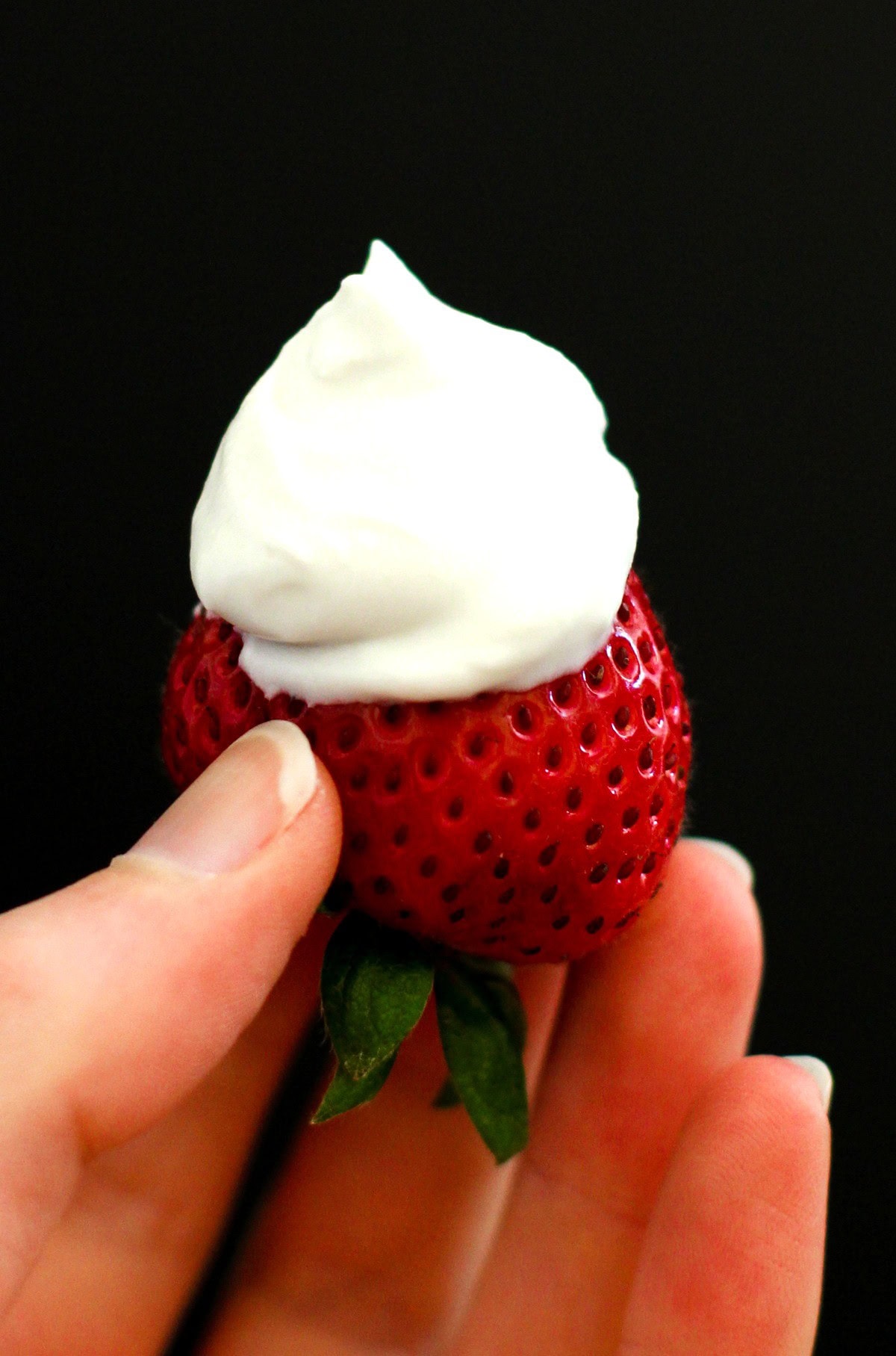 Hand holding a strawberry dipped in coconut whipped cream. Ready to eat.