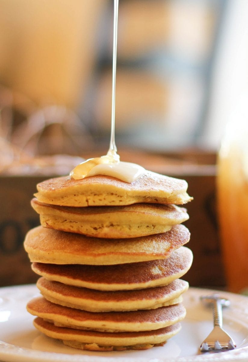 Stack of cornbread pancakes on a plate with honey drizzling on top with a fork to the side.