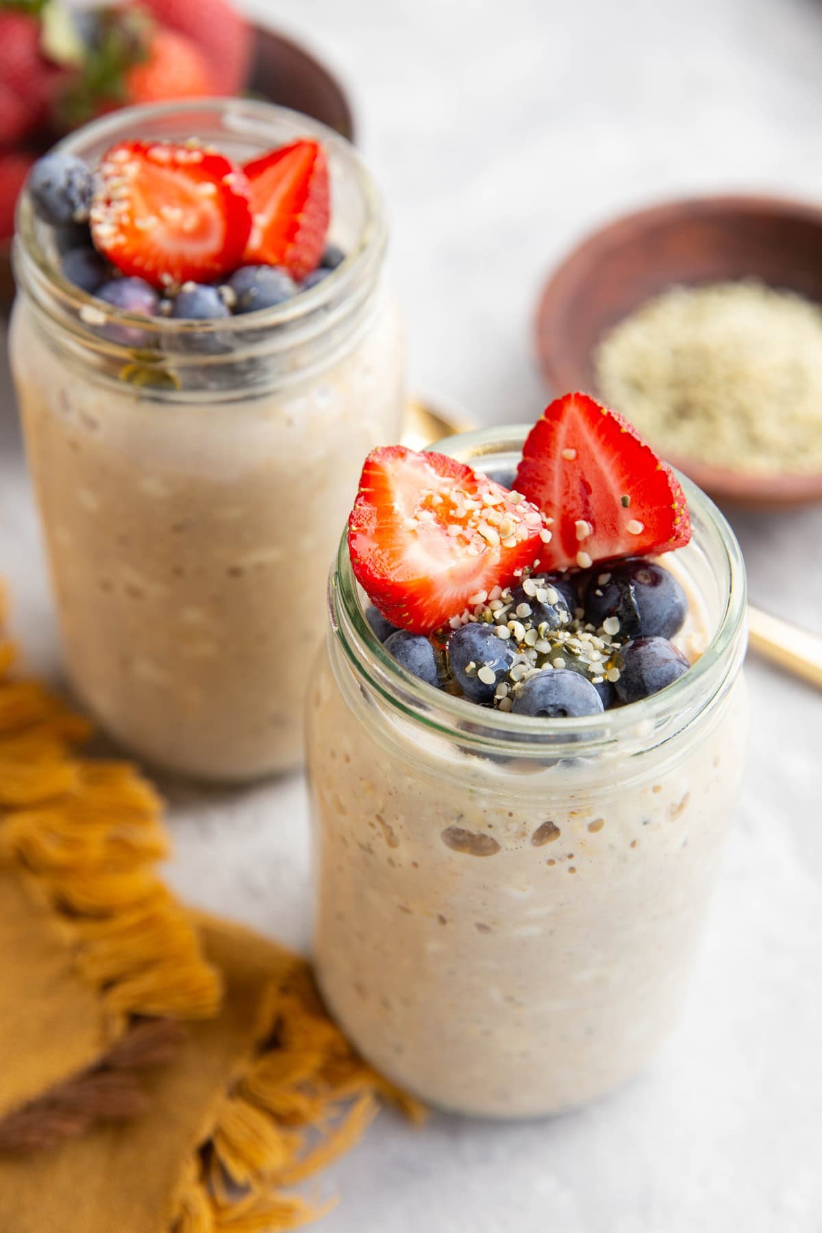 Two jars filled with cottage cheese overnight oats with fresh blueberries, chopped strawberries and honey on top.