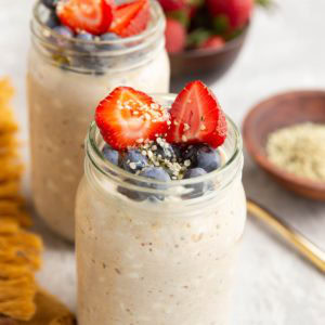 Two jars full of cottage cheese overnight oats with fresh fruit on top and a bowl of strawberries in the background.