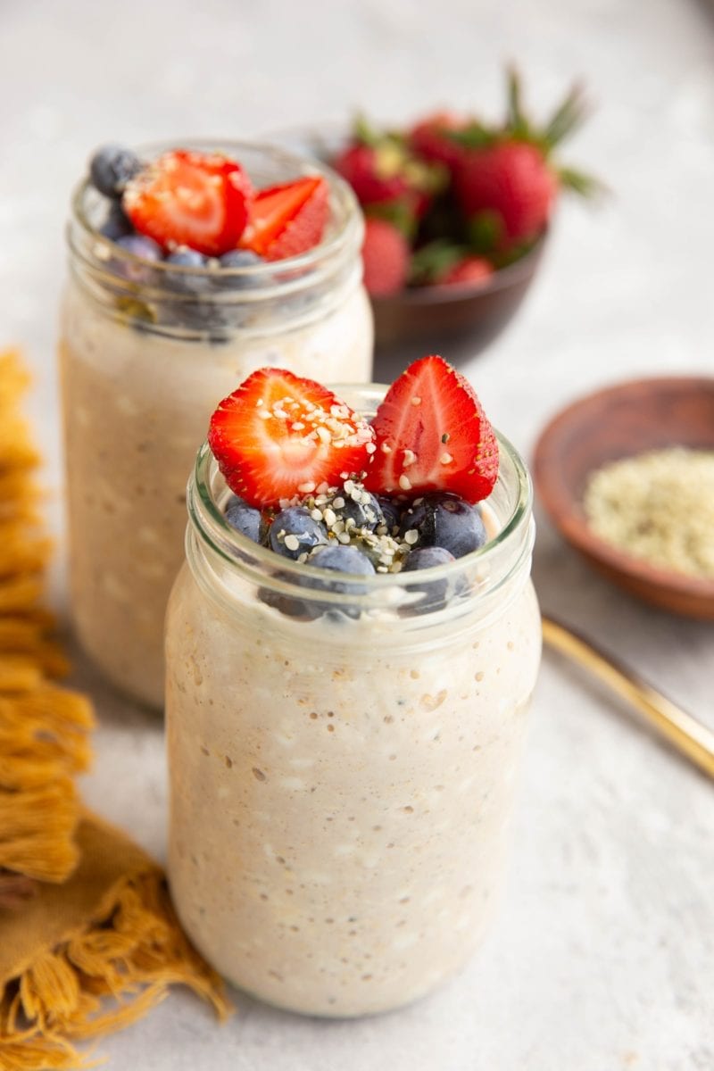 Two jars full of cottage cheese overnight oats with fresh fruit on top and a bowl of strawberries in the background.