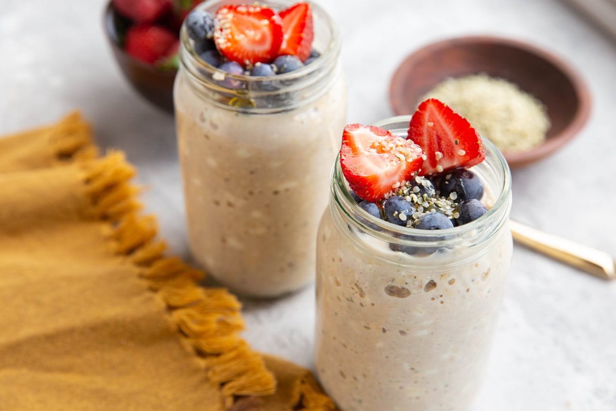 Two mason jars full of cottage cheese overnight oats with fresh berries and hemp seeds on top.