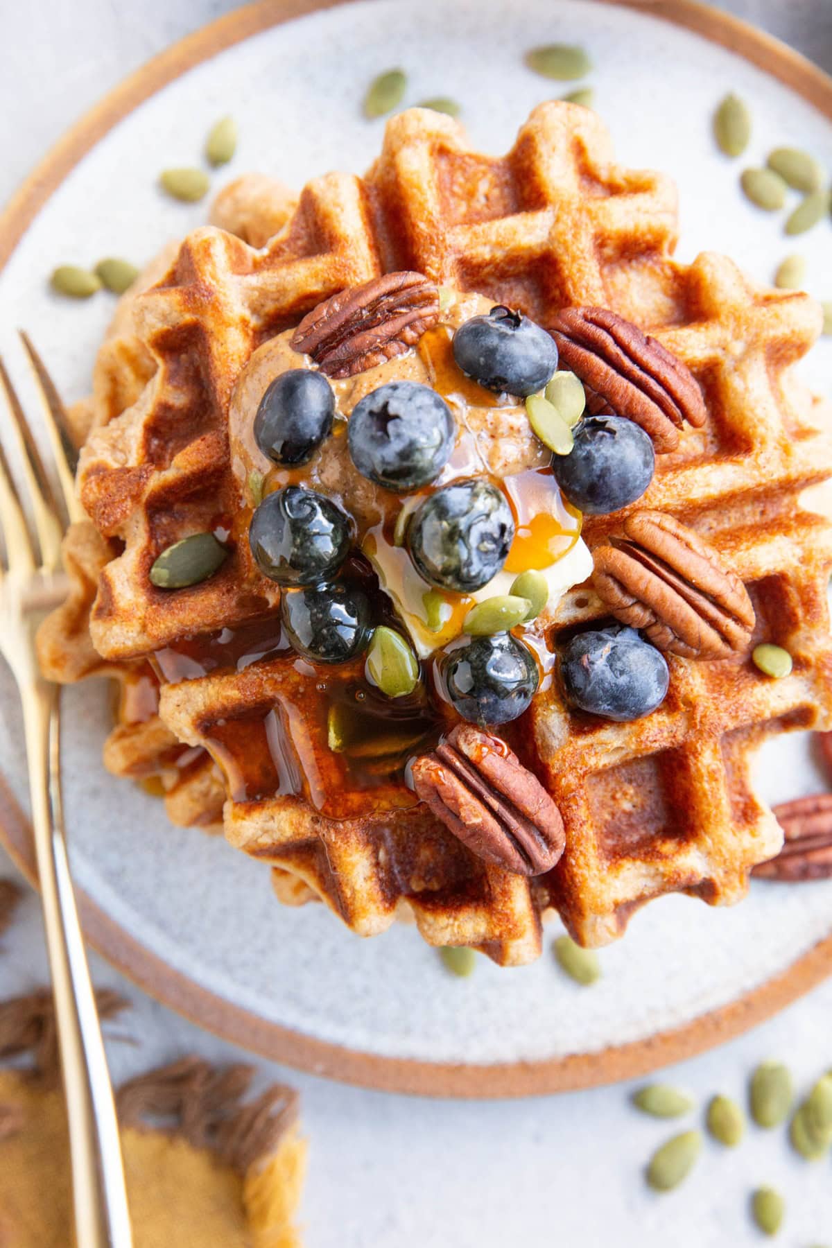 Waffles with butter, almond butter, blueberries, pecans and pumpkin seeds on top.