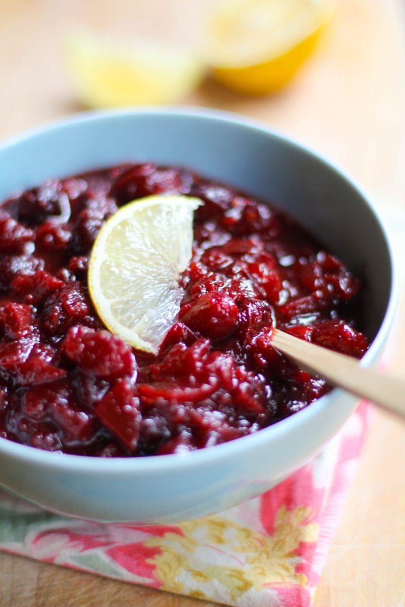 Cranberry Sauce with Ginger and Maple recipe inside of a blue bowl sitting on top of a pretty napkin and a cutting board.