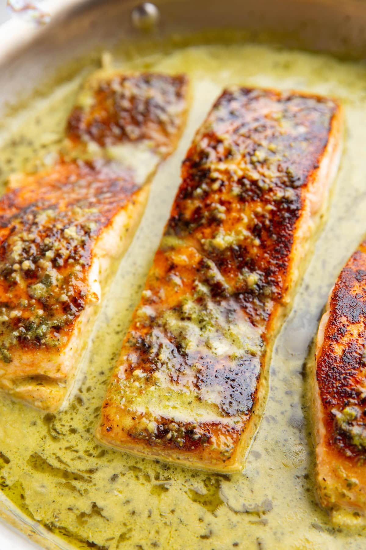 Skillet full of seared salmon with creamy pesto sauce.