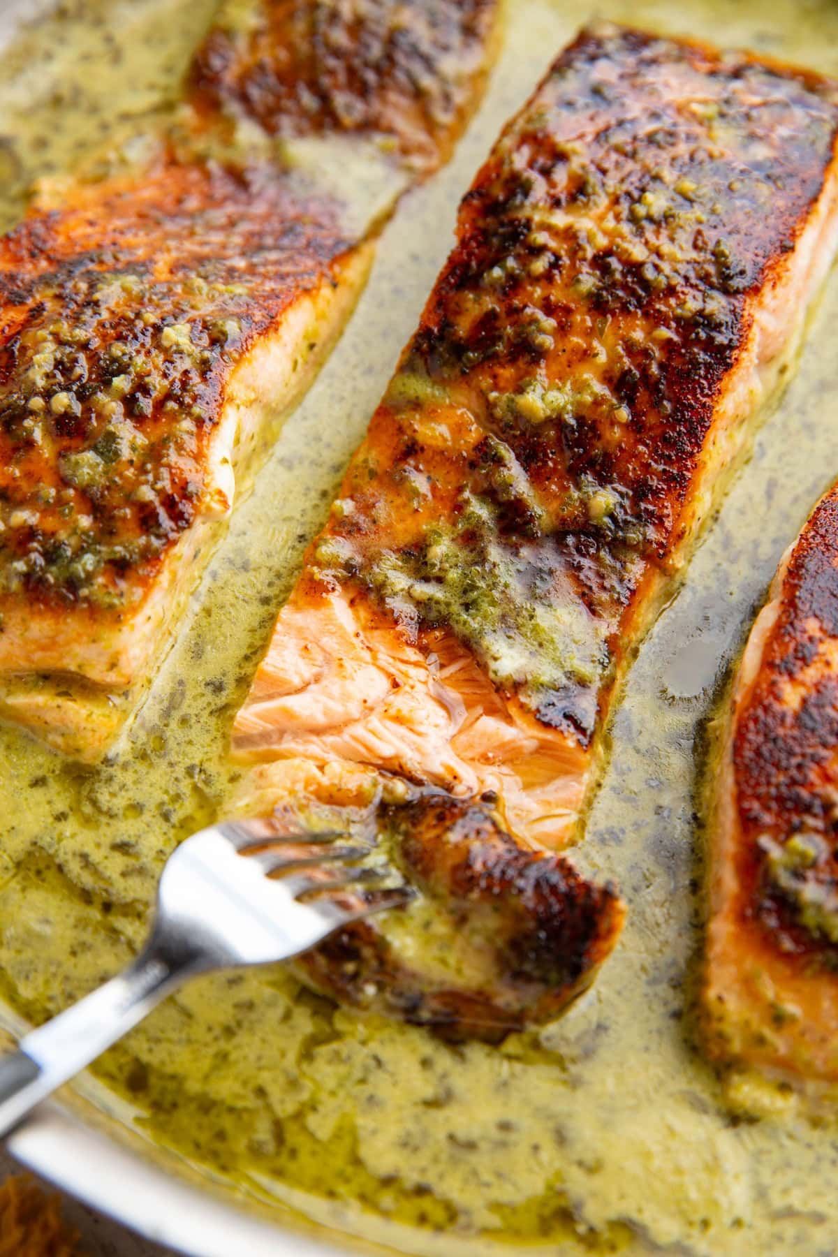 Skillet of salmon filets with a fork flaking the salmon to reveal the inside.