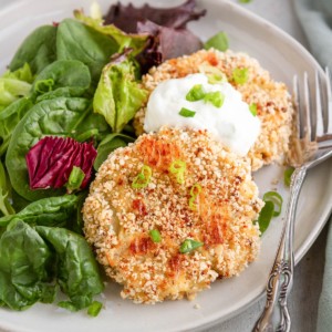 Cauliflower potato cakes on a white plate with a side salad, ready to serve.