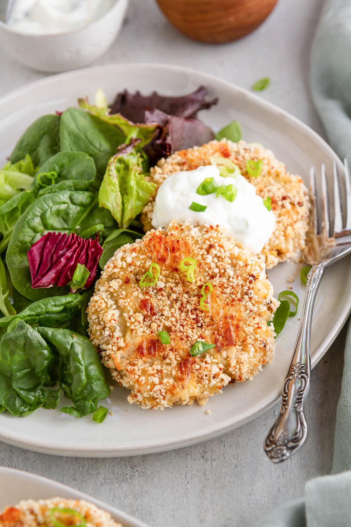 Cauliflower potato cakes on a white plate with a side salad, ready to serve.
