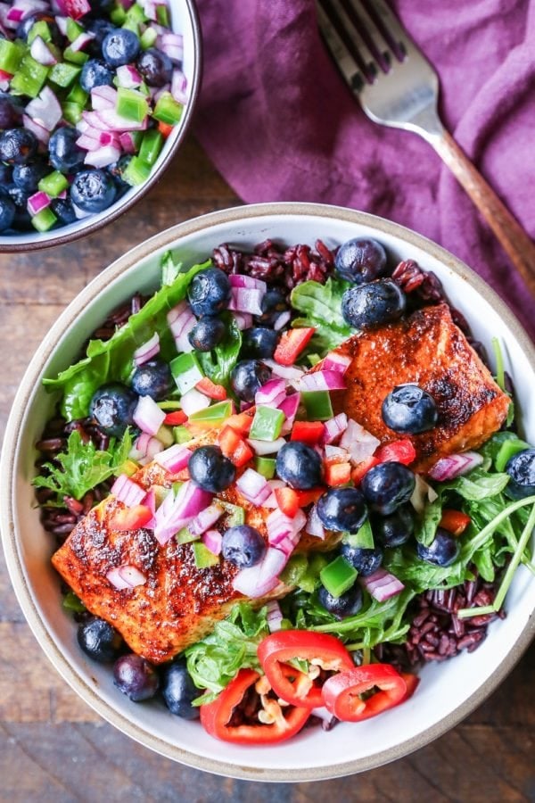 Bowl of crispy salmon on a bed of salad with blueberry salsa on top.