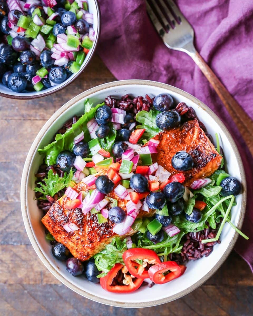 Bowl of crispy salmon on a bed of salad with blueberry salsa on top.