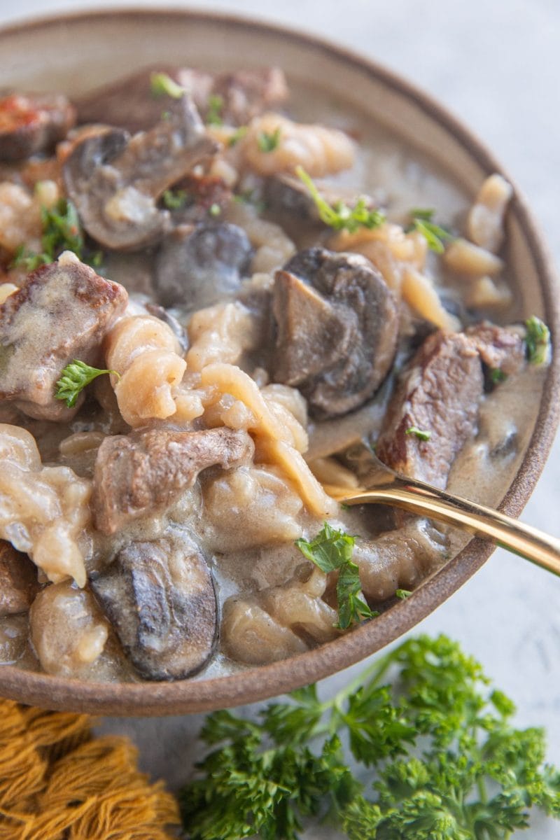 Big bowl of beef stroganoff. with a golden fork inside and fresh parsley to the side.