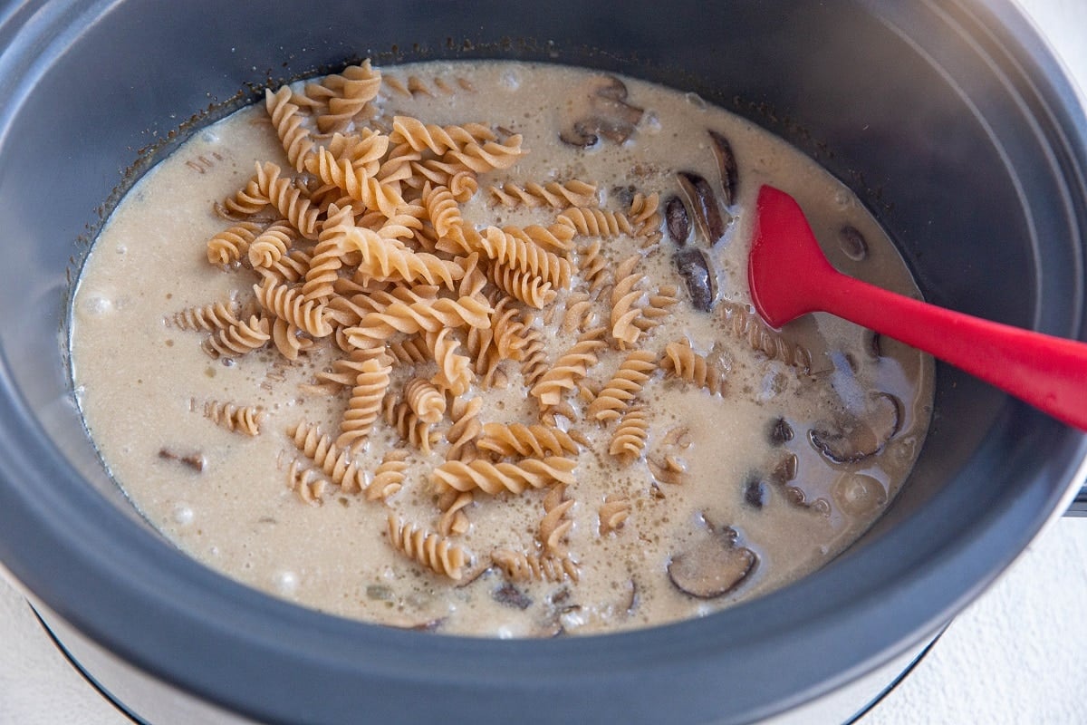 Pasta noodles being stirred into a crock pot.