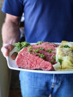 Man holding a plate of corned beef and cabbage, ready to serve.