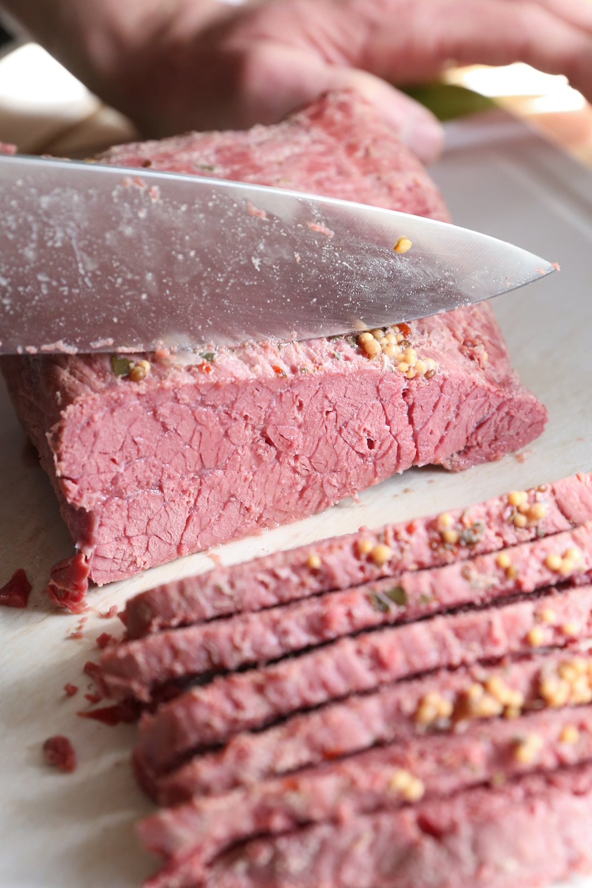Corned beef on a cutting board, being cut into slices using a sharp knife.