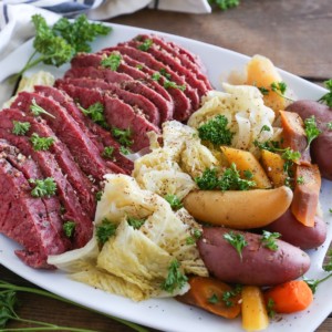White platter of sliced corned beef, cabbage, and potatoes on a wooden table.