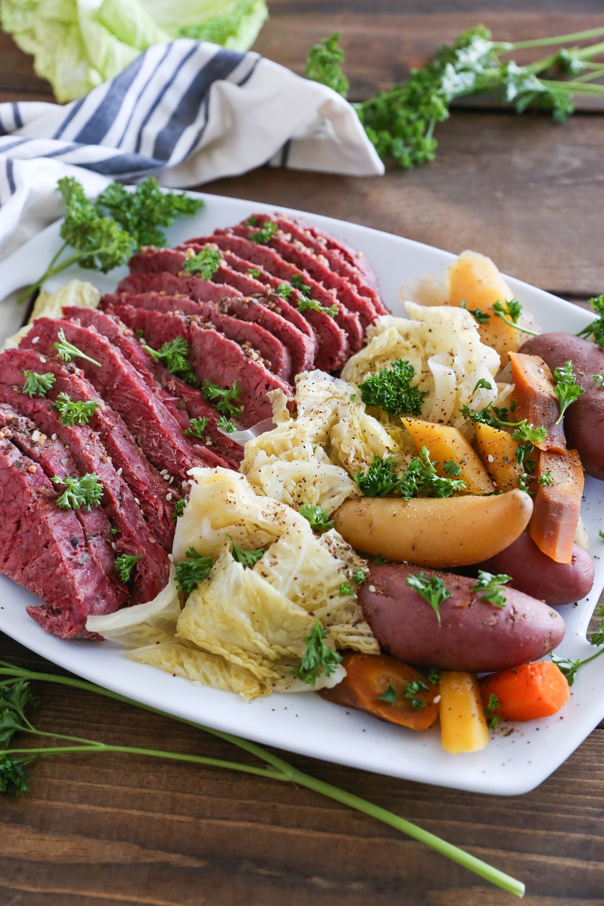 White platter of sliced corned beef, cabbage, and potatoes on a wooden table.